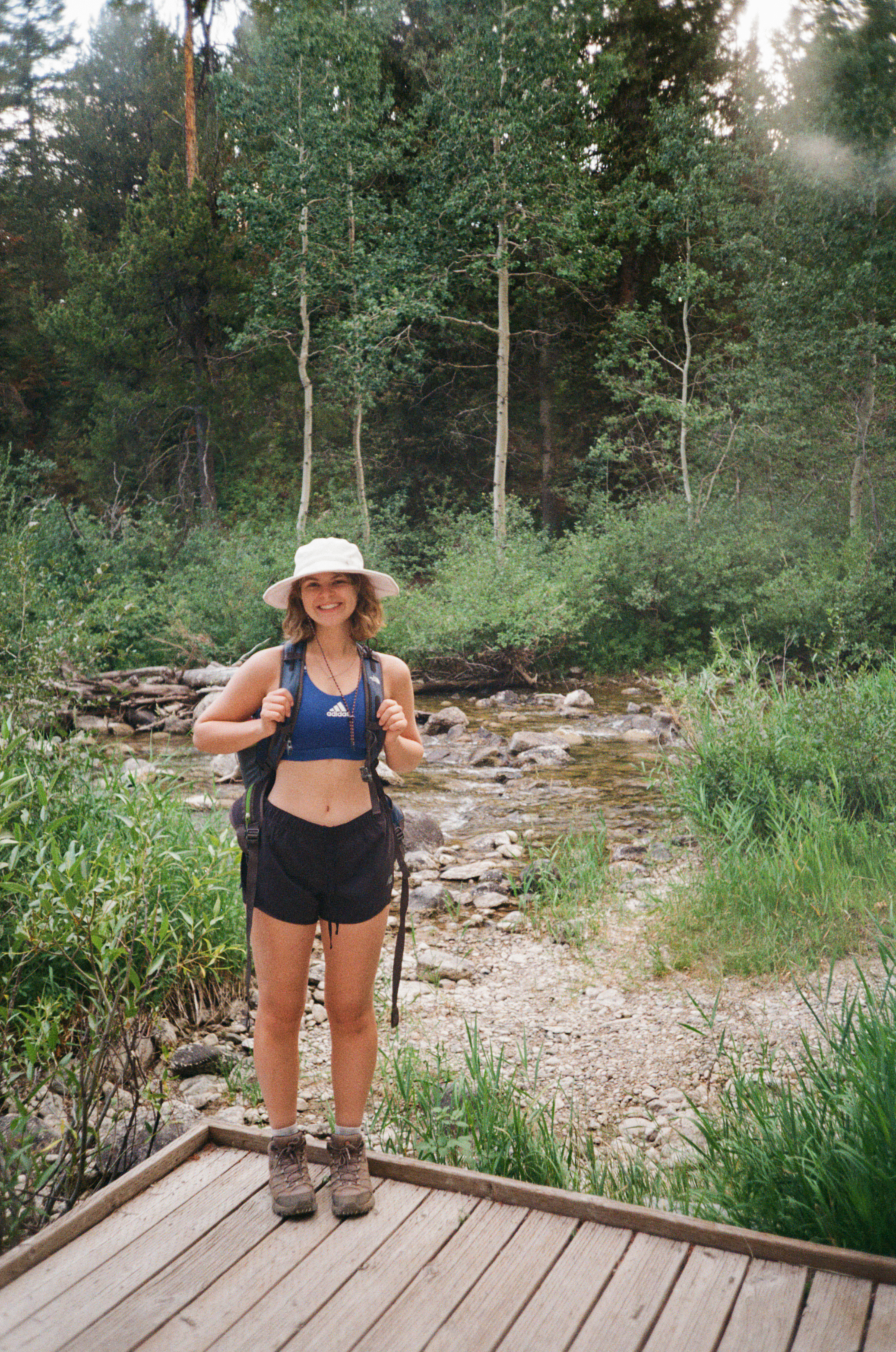 Claire hiking beside a stream, wearing a sun hat and backpack